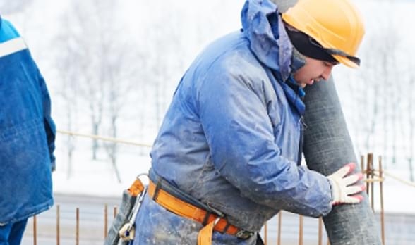 Construction worker wearing winter gear handling materials in cold weather for safe construction work conditions.