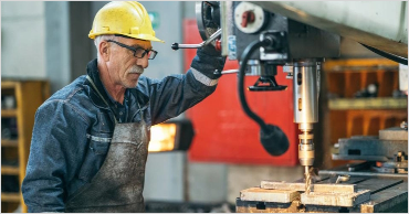 Experienced industrial worker operating drill press machine in manufacturing workshop