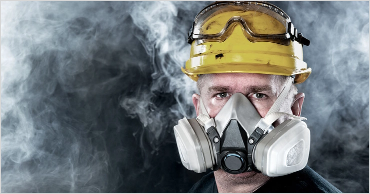 Worker wearing respirator mask and safety helmet for protection against airborne workplace hazards and respiratory safety awareness.