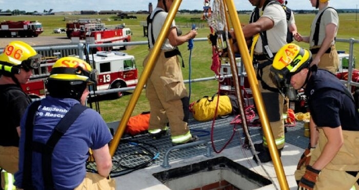 Rescue team practicing confined space entry and rescue procedure using tripod system during safety training