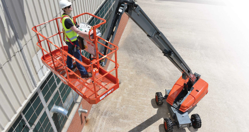 Worker operating a boom lift during aerial lift and mobile elevating work platform training near building exterior.