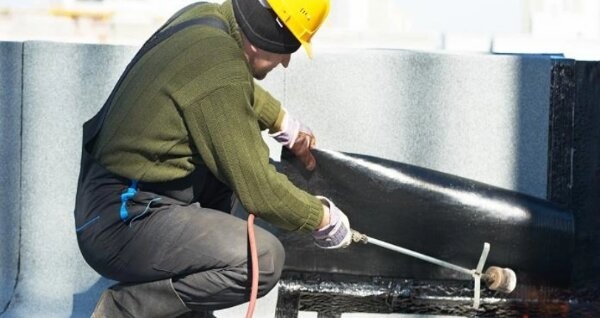 Construction worker operating propane torch on roofing surface during propane safety training in construction.
